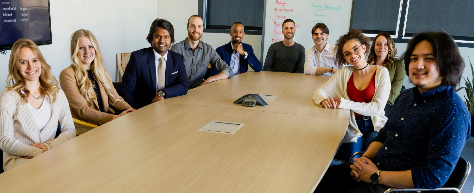 a board room with people of all races sitting around smiling at the camera
